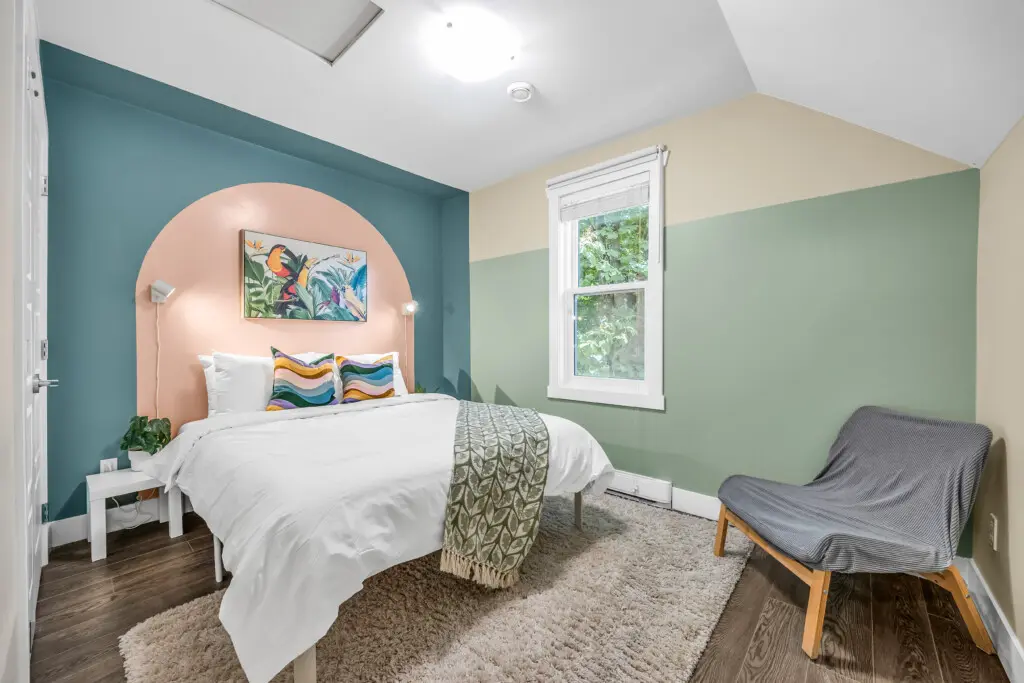 Bright and inviting second bedroom featuring a cozy queen bed and plenty of natural light streaming through the large window — a perfect spot to relax and recharge.