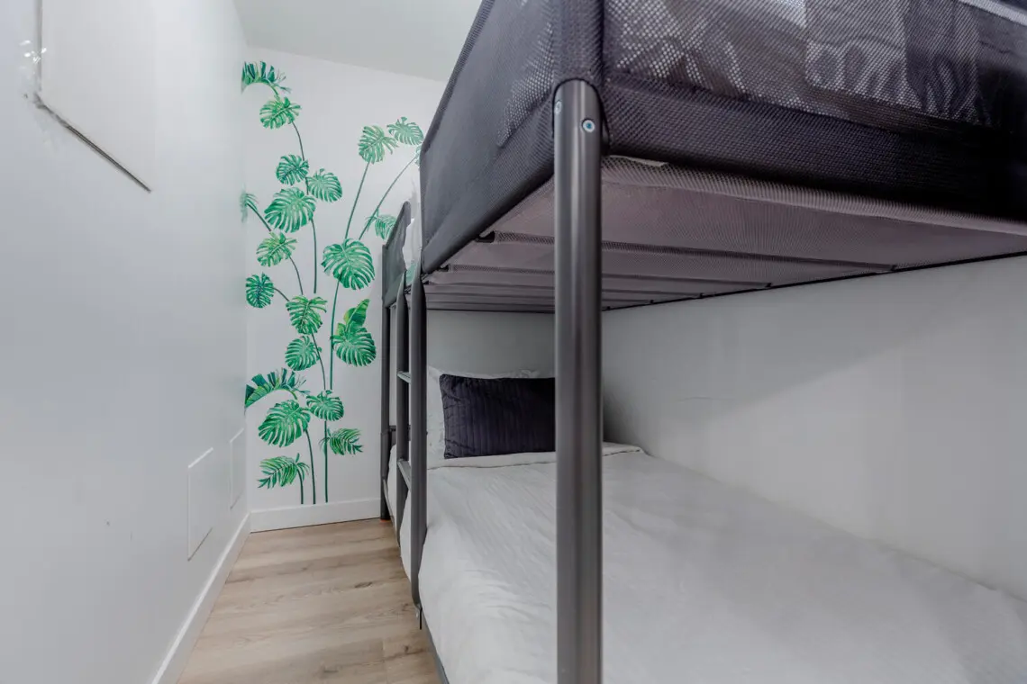 A thoughtfully designed bunk space with clean lines and a soft, modern palette offers a cozy and practical sleeping setup. The subtle botanical mural adds a touch of character, creating a calm retreat ideal for longer stays.