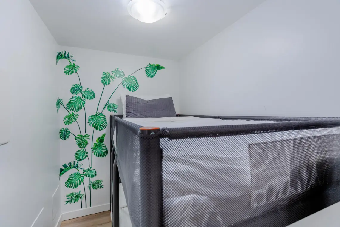 A thoughtfully designed bunk space with clean lines and a soft, modern palette offers a cozy and practical sleeping setup. The subtle botanical mural adds a touch of character, creating a calm retreat ideal for longer stays.