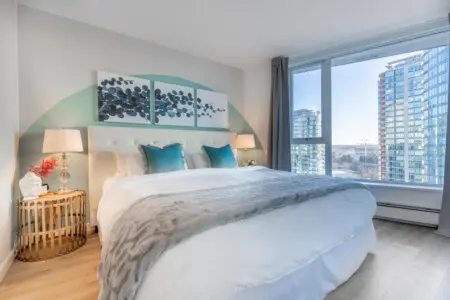 Rest easy in the serene main bedroom, featuring a plush king bed and floor-to-ceiling windows with city views. Soft tones and blackout curtains create a peaceful retreat in the heart of Vancouver.