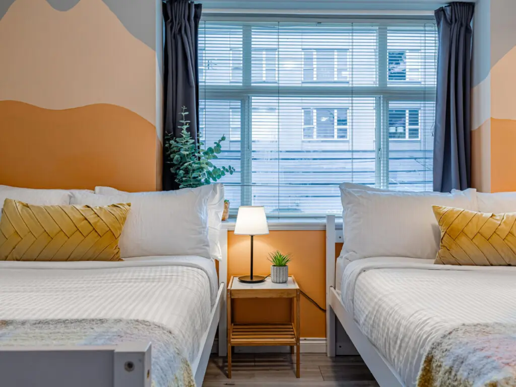 The second bedroom features two cozy double beds with soft linens and warm accents, creating a bright and restful space for families or friends to unwind after a day in Vancouver