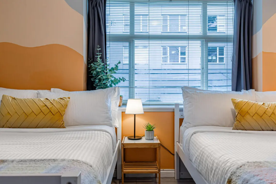 The second bedroom features two cozy double beds with soft linens and warm accents, creating a bright and restful space for families or friends to unwind after a day in Vancouver