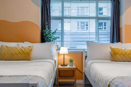 The second bedroom features two cozy double beds with soft linens and warm accents, creating a bright and restful space for families or friends to unwind after a day in Vancouver