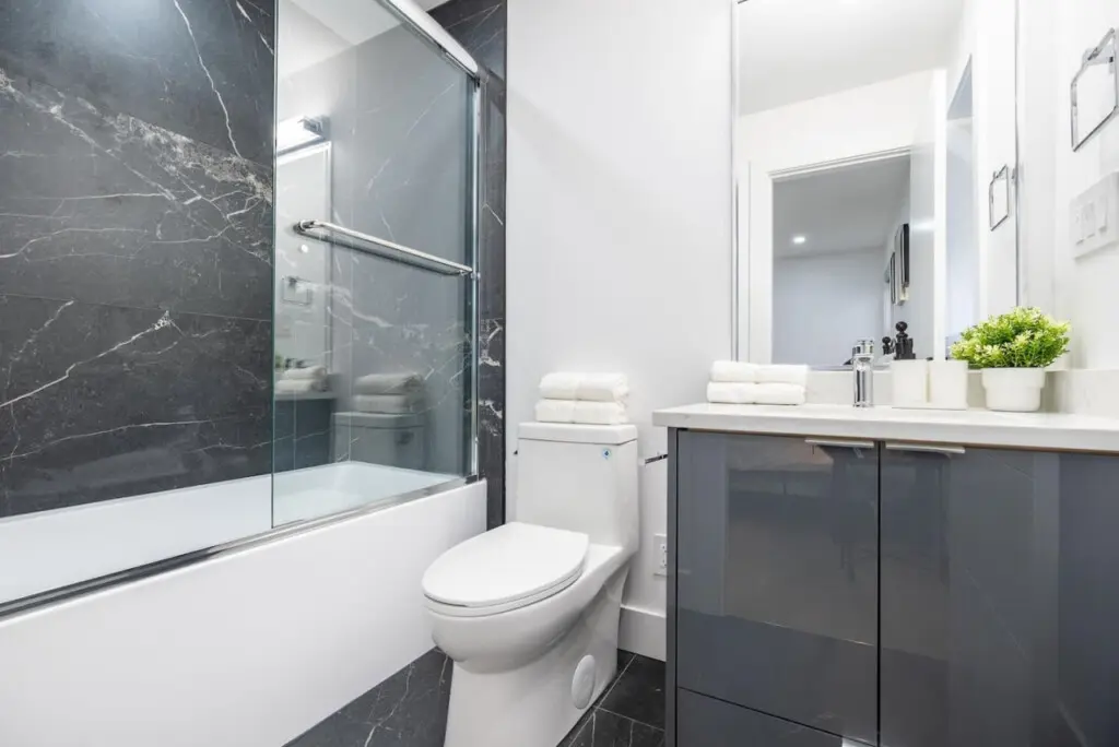 Connected to the main-floor bedroom, this private ensuite features dark marble-inspired tiles, a glass-enclosed bathtub, and a modern vanity — offering guests a stylish and comfortable space to unwind.