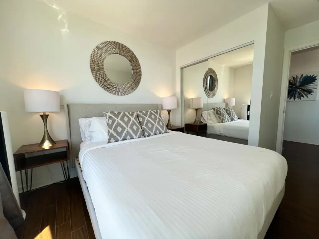 A cozy and stylish bedroom featuring a plush bed, elegant lighting, and a mirrored closet that enhances the sense of space. Designed for relaxation and restful nights in a calm, modern setting.