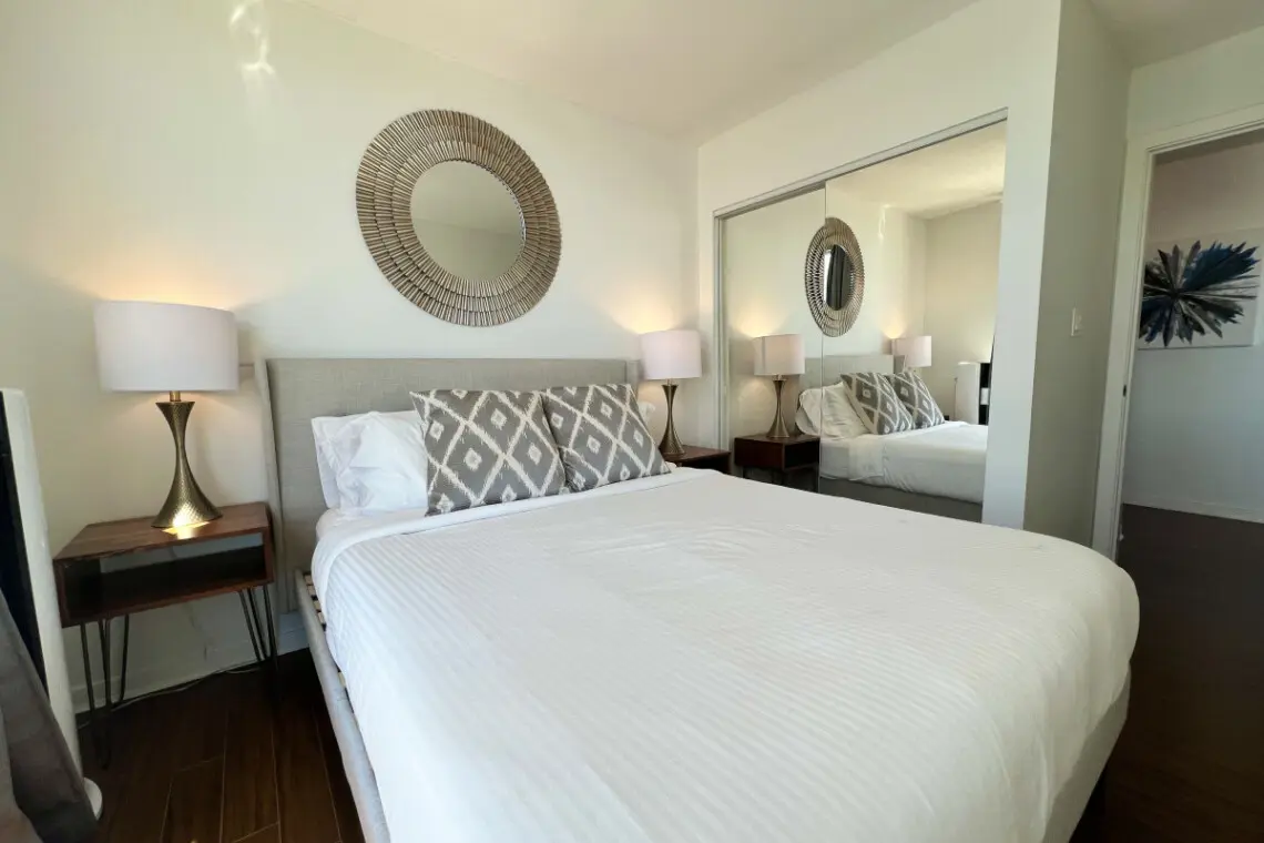 A cozy and stylish bedroom featuring a plush bed, elegant lighting, and a mirrored closet that enhances the sense of space. Designed for relaxation and restful nights in a calm, modern setting.