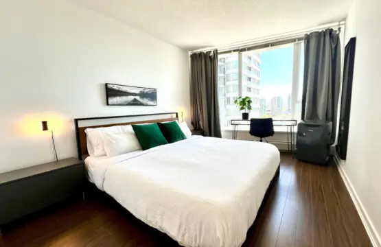 Unwind in the serene comfort of the primary bedroom, featuring a plush king bed, warm lighting, and floor-to-ceiling windows with city views. A peaceful space designed for rest, relaxation, and quiet moments after a day exploring Vancouver.