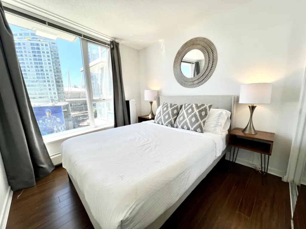 Settle into modern comfort in this bright bedroom, where plush bedding, elegant decor, and city views combine to create a restful urban sanctuary.