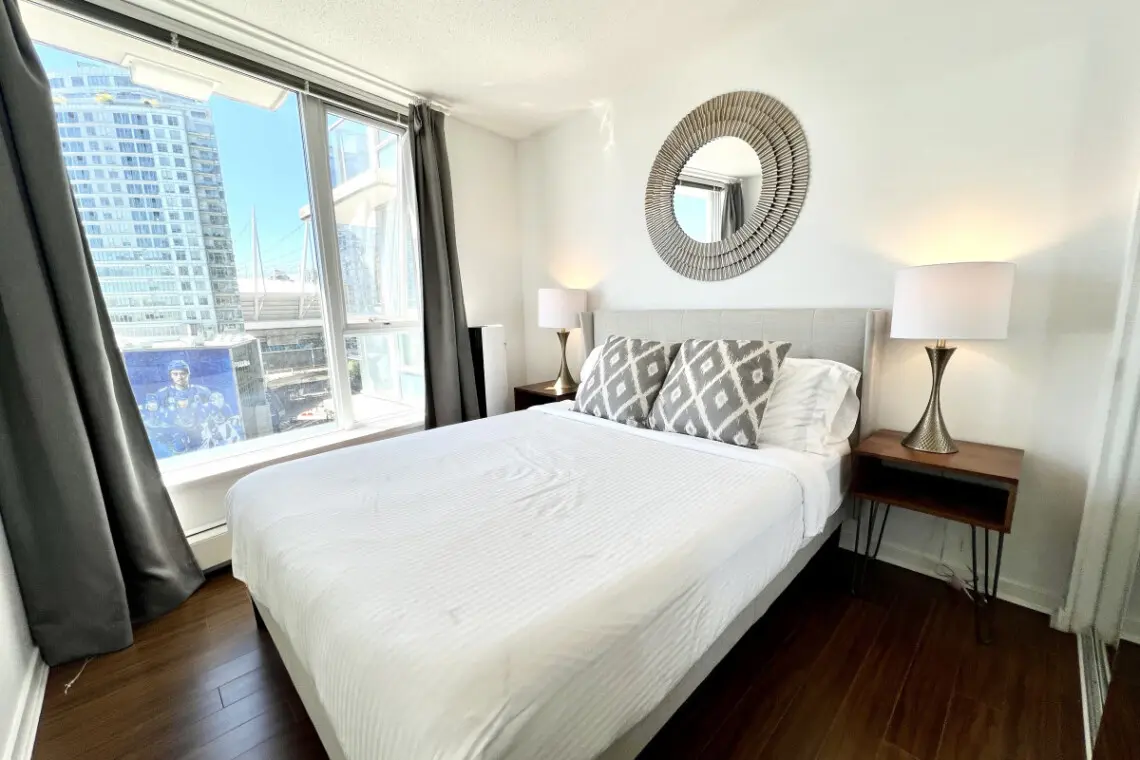 Settle into modern comfort in this bright bedroom, where plush bedding, elegant decor, and city views combine to create a restful urban sanctuary.