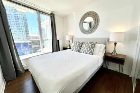 Settle into modern comfort in this bright bedroom, where plush bedding, elegant decor, and city views combine to create a restful urban sanctuary.