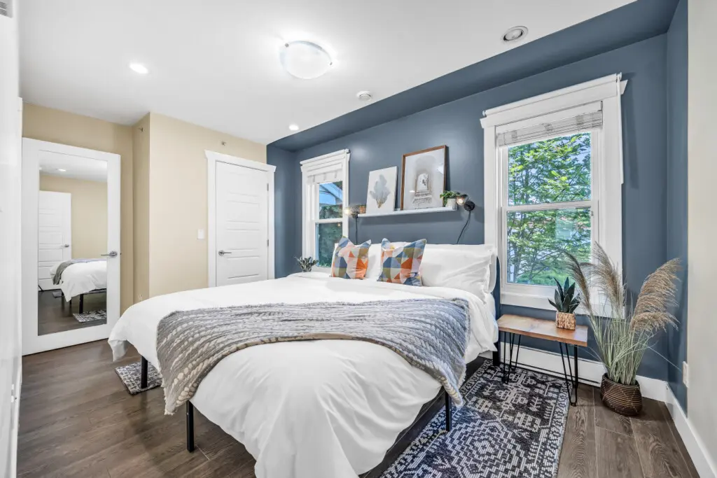 Bright and stylish main bedroom (Bedroom 1) featuring a cozy queen bed, modern accents, and plenty of natural light streaming through large windows for a calm and refreshing ambiance.