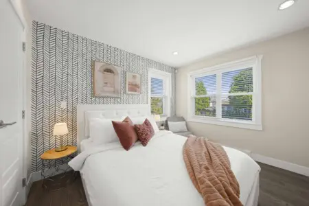 This bright second bedroom offers a peaceful retreat with a plush queen bed, soft linens, and warm accents. Large windows fill the space with natural light and views of the quiet neighborhood — perfect for restful nights and relaxed mornings.