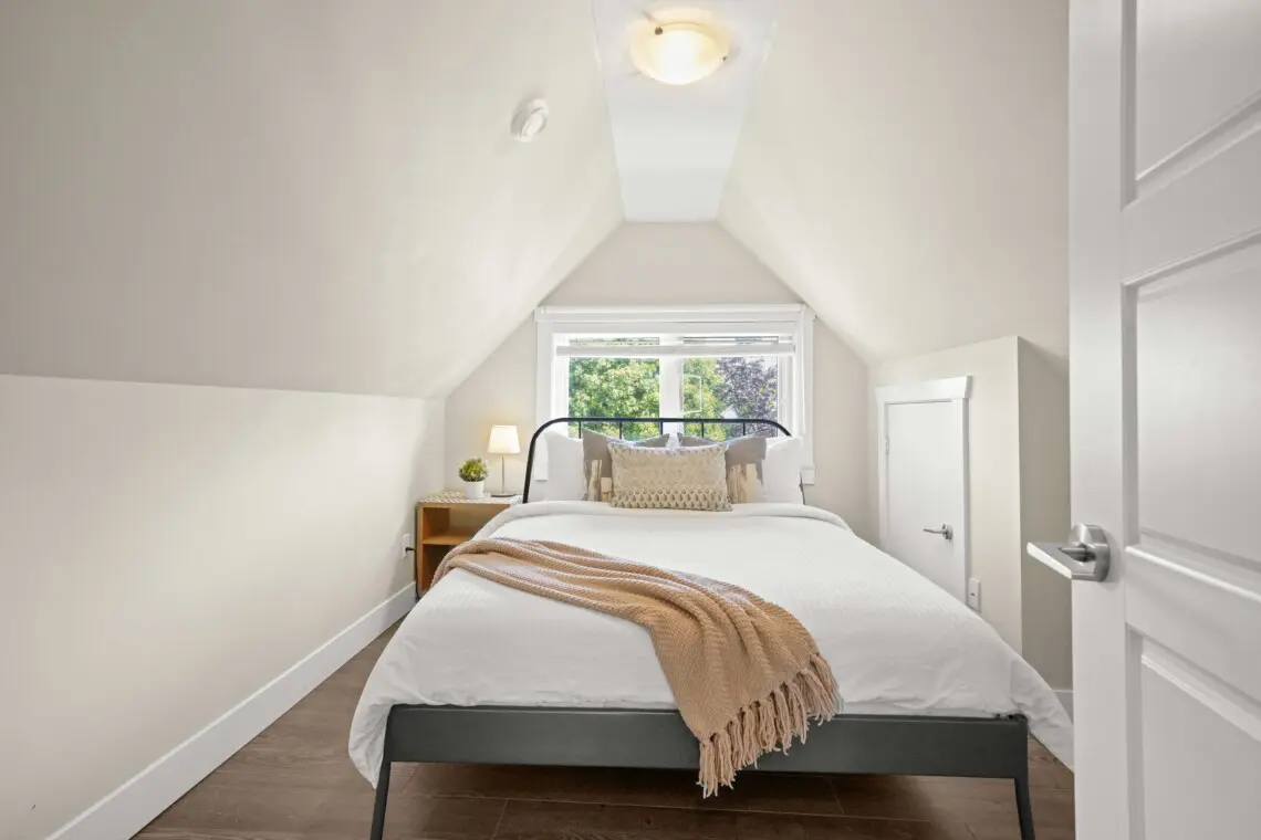 Tucked beneath charming vaulted ceilings, the third-floor bedroom offers a cozy and private retreat. A plush queen bed, soft lighting, and warm neutral tones create a peaceful atmosphere — perfect for unwinding after a day in the city.