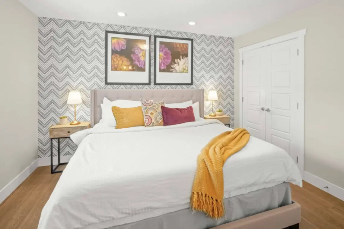 The primary bedroom offers a peaceful retreat with a plush king bed, soft linens, and blackout blinds for restful sleep. Warm lighting and colorful accents add a cozy, modern touch — perfect for unwinding after a day in the city.