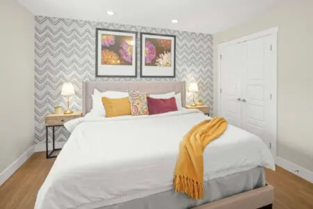 The primary bedroom offers a peaceful retreat with a plush king bed, soft linens, and blackout blinds for restful sleep. Warm lighting and colorful accents add a cozy, modern touch — perfect for unwinding after a day in the city.