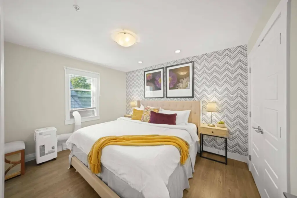 The primary bedroom offers a serene retreat with a plush king bed dressed in crisp white linens and soft accent pillows. Filled with natural light and calming tones, it’s the perfect space to unwind after a day in the city.