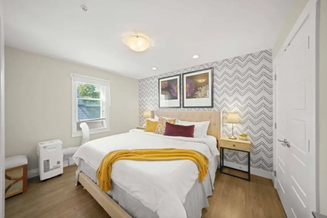 The primary bedroom offers a serene retreat with a plush king bed dressed in crisp white linens and soft accent pillows. Filled with natural light and calming tones, it’s the perfect space to unwind after a day in the city.