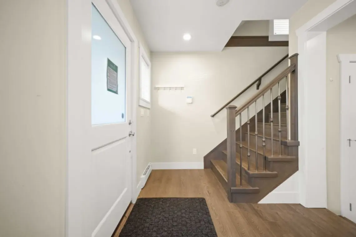 A bright and inviting entryway welcomes guests with soft natural light and warm wood finishes, setting a relaxed tone from the moment they arrive. The staircase leads to the home’s upper level, offering a smooth transition from shared spaces to private re