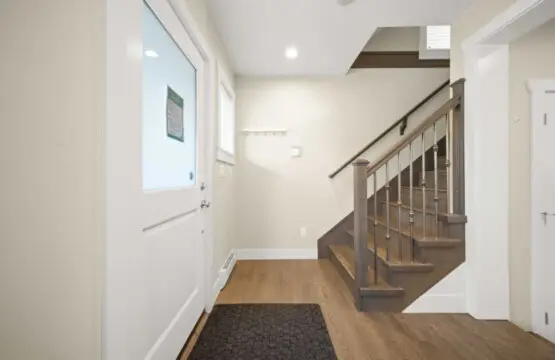 A bright and inviting entryway welcomes guests with soft natural light and warm wood finishes, setting a relaxed tone from the moment they arrive. The staircase leads to the home’s upper level, offering a smooth transition from shared spaces to private re