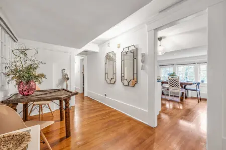 A charming entryway featuring a vintage-inspired table with decorative vases, framed mirrors, and a warm wooden floor, creating a welcoming atmosphere.