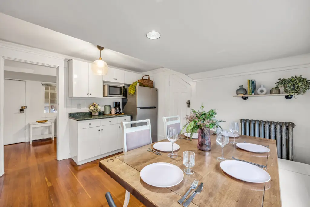 A cozy dining area with a charming wooden table, four seats, and a simple yet stylish design, featuring natural light and kitchen amenities for a relaxing meal experience.