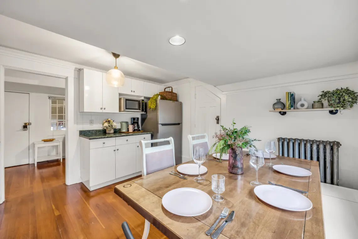 A cozy dining area with a charming wooden table, four seats, and a simple yet stylish design, featuring natural light and kitchen amenities for a relaxing meal experience.