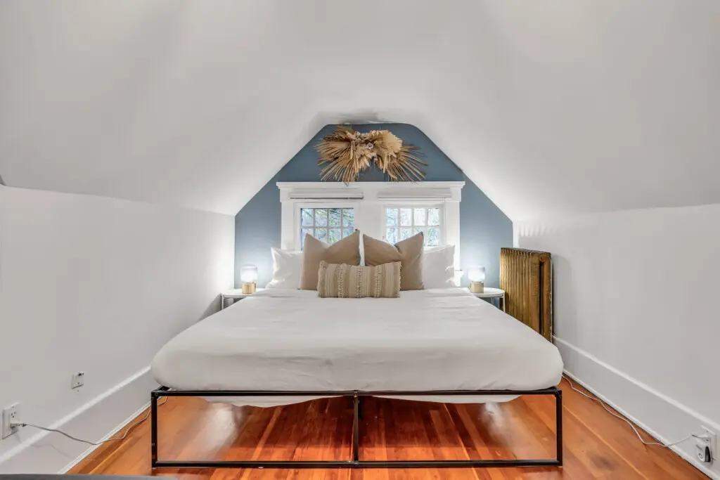 A serene bedroom with a cozy bed, soft lighting, and a charming accent wall, offering a peaceful retreat with natural light from the windows.