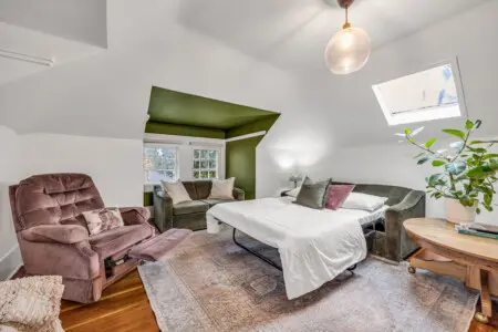 A cozy and inviting room featuring a plush recliner, comfortable seating, and a spacious bed, perfect for relaxation with natural light streaming in from the windows.