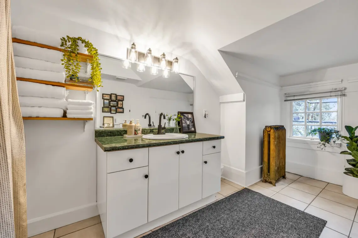 A spacious bathroom featuring a sleek green countertop, floating shelves stocked with fresh towels, and large windows for natural light.