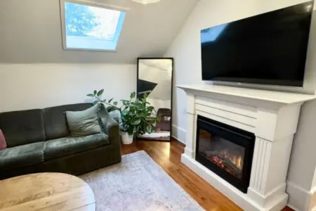 A cozy living space featuring a plush sofa, a warm fireplace, and natural light pouring in through the skylight, creating a welcoming atmosphere.