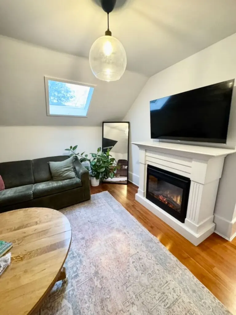 A cozy living space featuring a plush sofa, a warm fireplace, and natural light pouring in through the skylight, creating a welcoming atmosphere.
