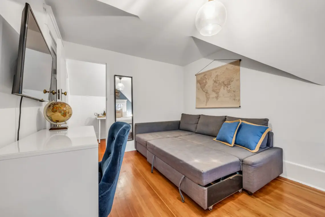 A cozy room featuring a convertible sofa bed, a small workspace, and modern decor, perfect for relaxing or accommodating guests.