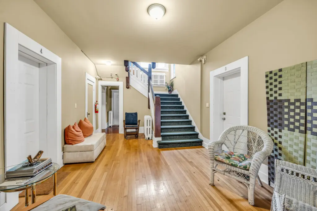 A welcoming hallway with warm wood floors, cozy seating, and a vintage-inspired staircase leading to the upper floors.