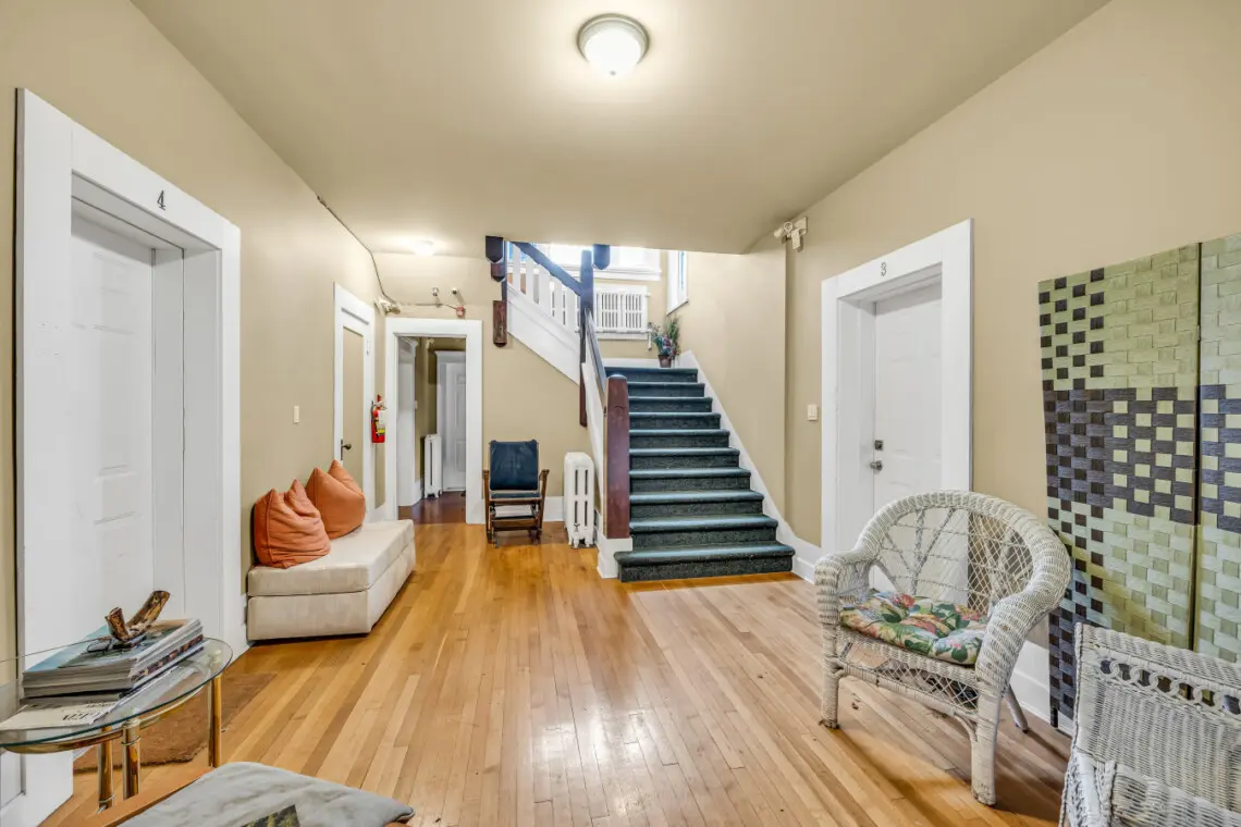 A welcoming hallway with warm wood floors, cozy seating, and a vintage-inspired staircase leading to the upper floors.