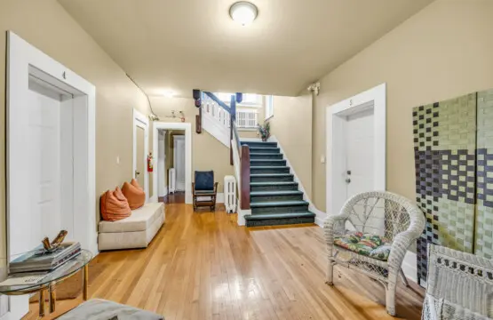 A welcoming hallway with warm wood floors, cozy seating, and a vintage-inspired staircase leading to the upper floors.