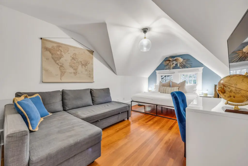 A bright and inviting living area with a cozy sectional sofa, a stylish work desk, and a peaceful bedroom nook with a world map above the bed.