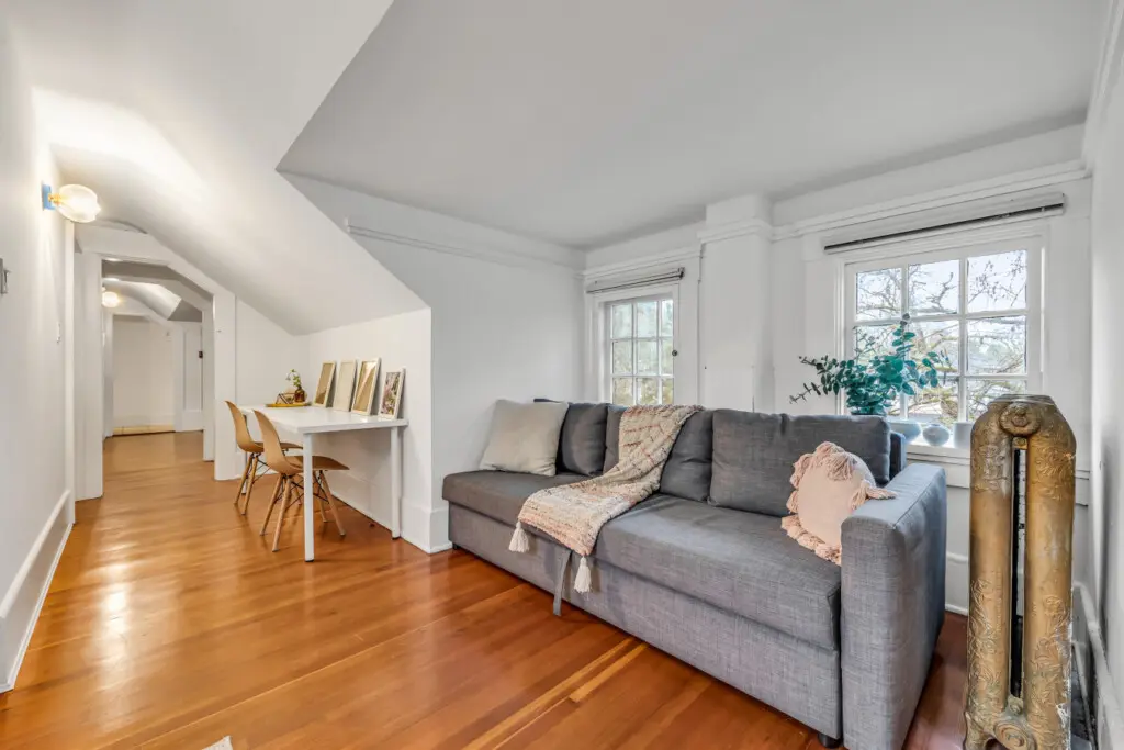 A cozy living space with a comfortable sofa, natural light streaming through the windows, and a work desk with framed art for a stylish, functional touch.