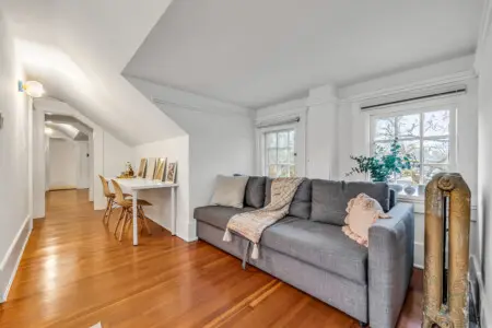 A cozy living space with a comfortable sofa, natural light streaming through the windows, and a work desk with framed art for a stylish, functional touch.