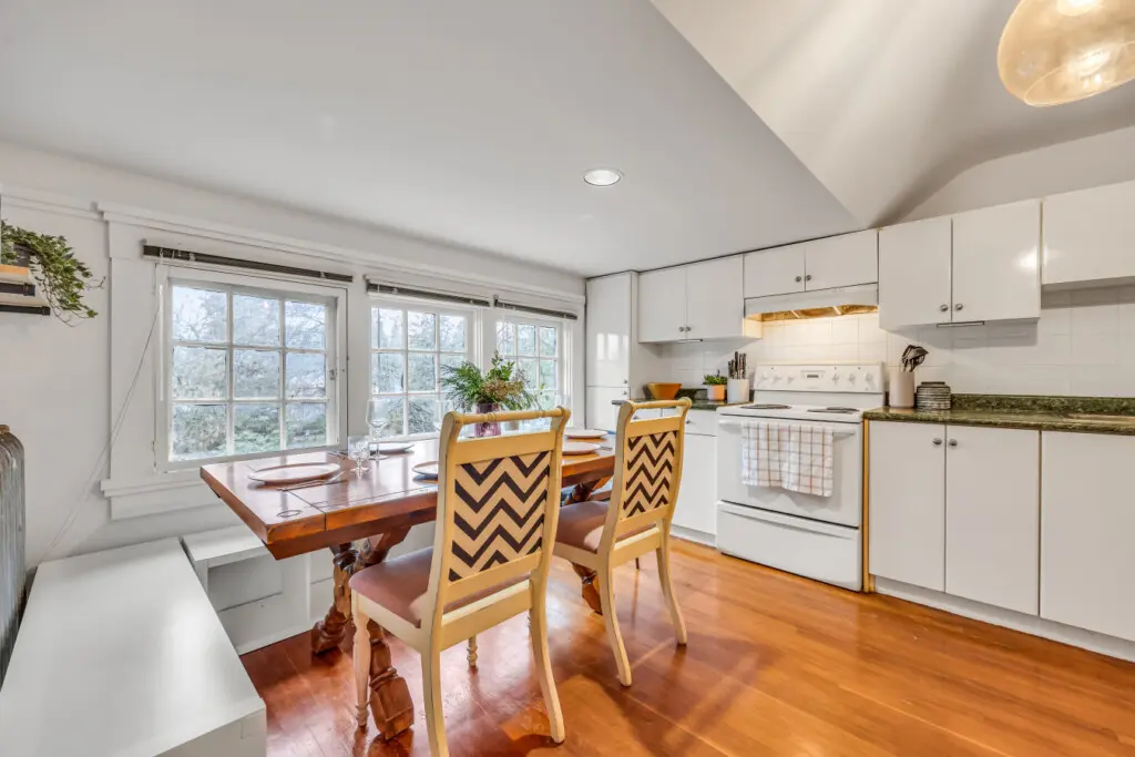 A spacious kitchen and dining area featuring a rustic wooden table, stylish chevron chairs, and large windows that bring in natural light, perfect for casual meals.