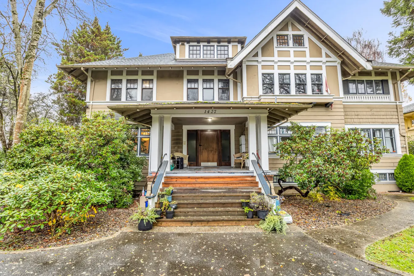 A large, stately house with an inviting porch, framed by lush greenery and well-maintained landscaping. The entrance features a set of stairs leading up to the front door, giving it a welcoming, classic charm.
