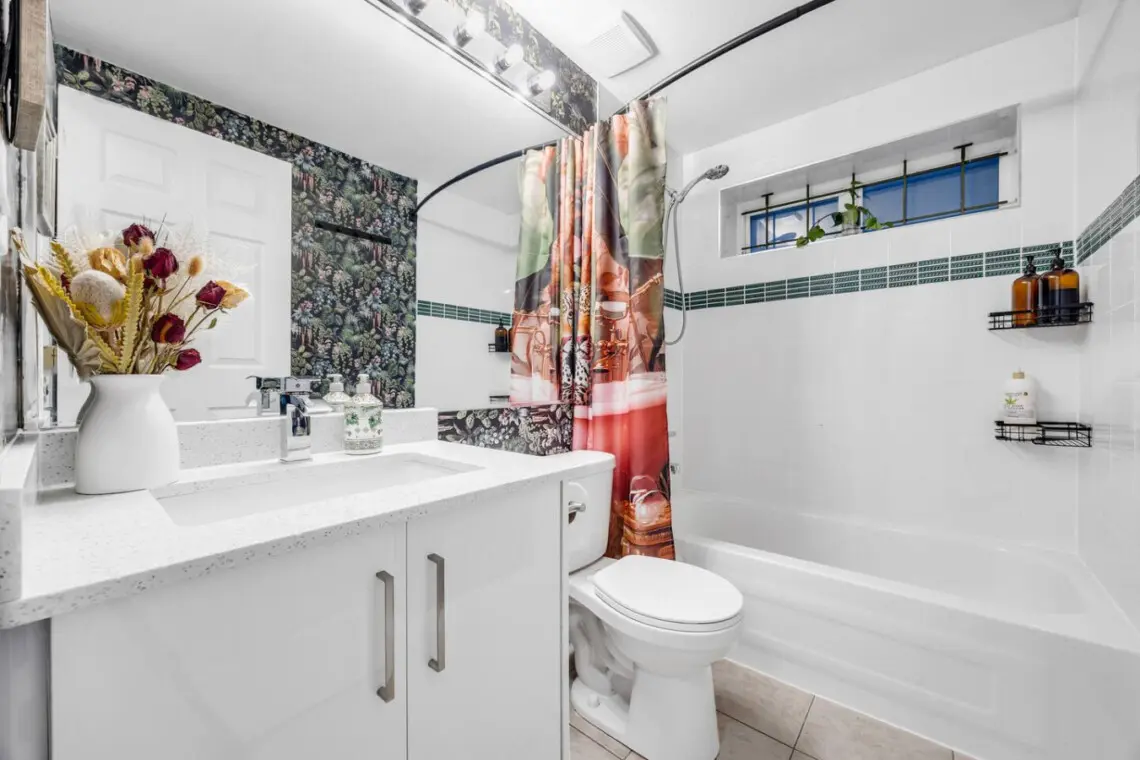 Fresh and vibrant bathroom with botanical wallpaper, modern fixtures, and a colorful shower curtain, offering a lively and functional space.