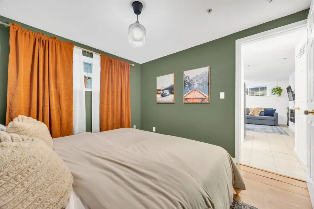 Cozy bedroom with earthy green walls, vibrant orange curtains, and a serene view of nature-inspired art, offering a peaceful and restful atmosphere.