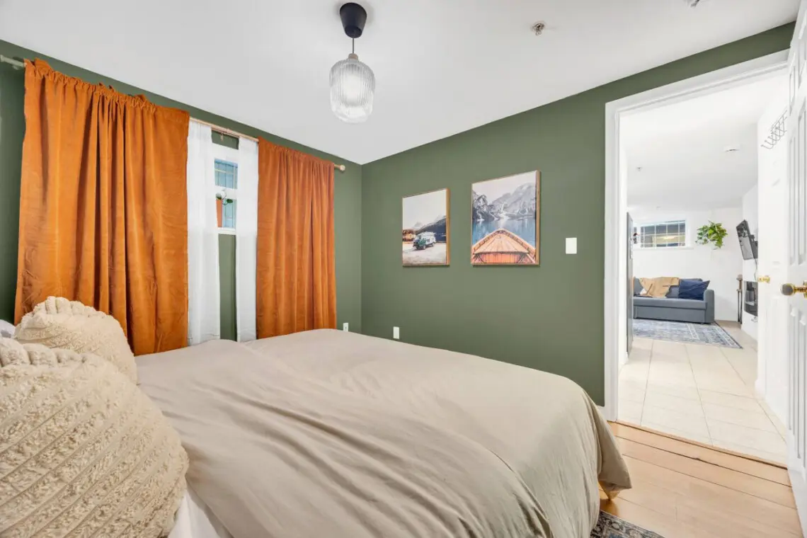 Cozy bedroom with earthy green walls, vibrant orange curtains, and a serene view of nature-inspired art, offering a peaceful and restful atmosphere.
