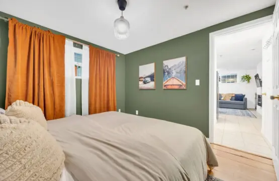 Cozy bedroom with earthy green walls, vibrant orange curtains, and a serene view of nature-inspired art, offering a peaceful and restful atmosphere.