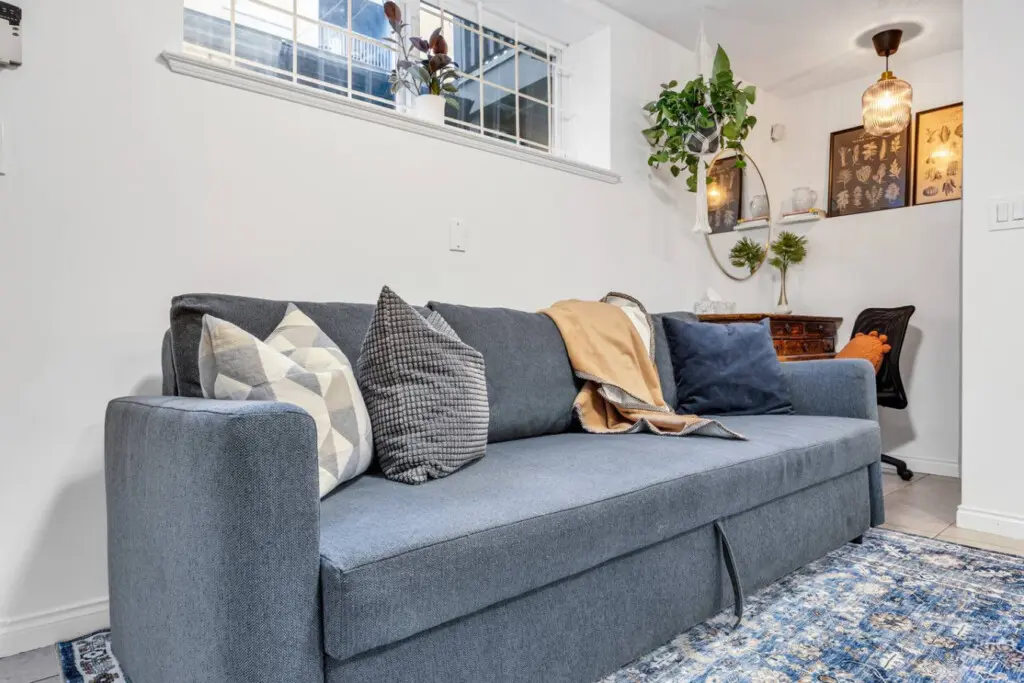 Cozy sofa adorned with decorative pillows and a soft throw, complemented by a stylish rug and plants, creating a welcoming and relaxed atmosphere.