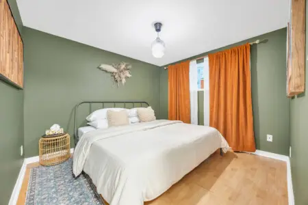 Cozy bedroom with a warm green accent wall, a comfortable bed, and stylish orange curtains, creating a peaceful and inviting space.