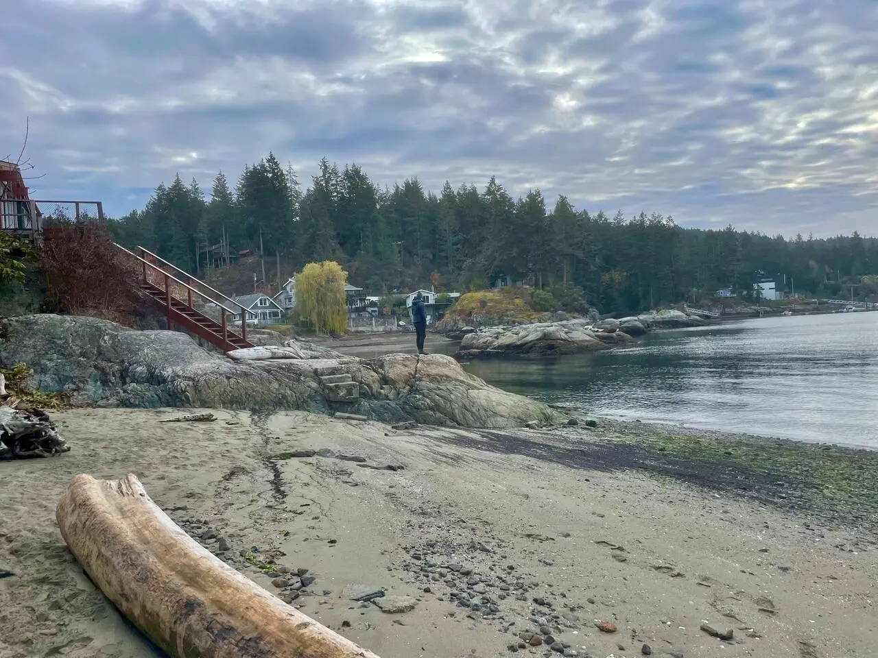 Peaceful beachside view with rocky shores, a wooden staircase, and a calm, scenic coastline, offering a tranquil escape by the water.