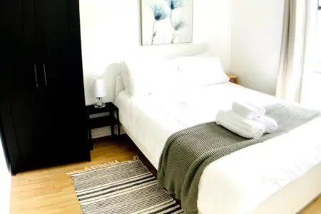 Bright, serene bedroom featuring a comfortable bed, stylish striped rug, and modern storage, creating a relaxing space with thoughtful details.