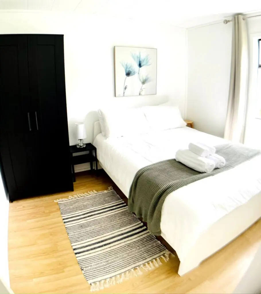Bright, serene bedroom featuring a comfortable bed, stylish striped rug, and modern storage, creating a relaxing space with thoughtful details.