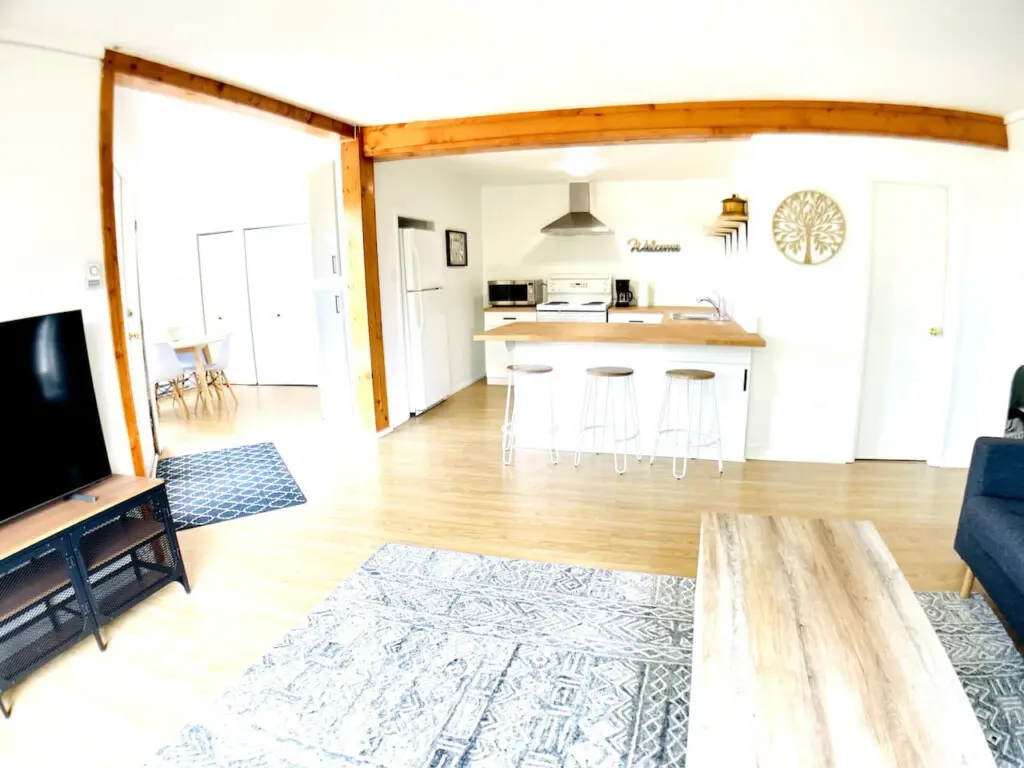 An open living and kitchen space with a breakfast bar, wooden accents, and bright natural light throughout.